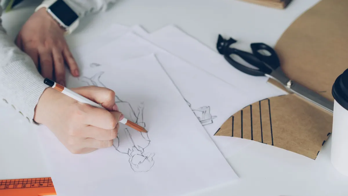 A designer sketching color and pattern concepts by hand at a studio desk, swatches and pencils in view