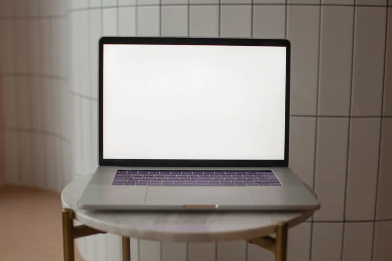 A laptop with a blank screen on a small round table, set up for a website mockup